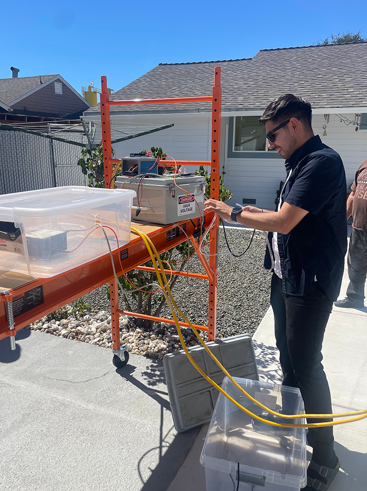 A person setting up wires into an instrument in front of a house