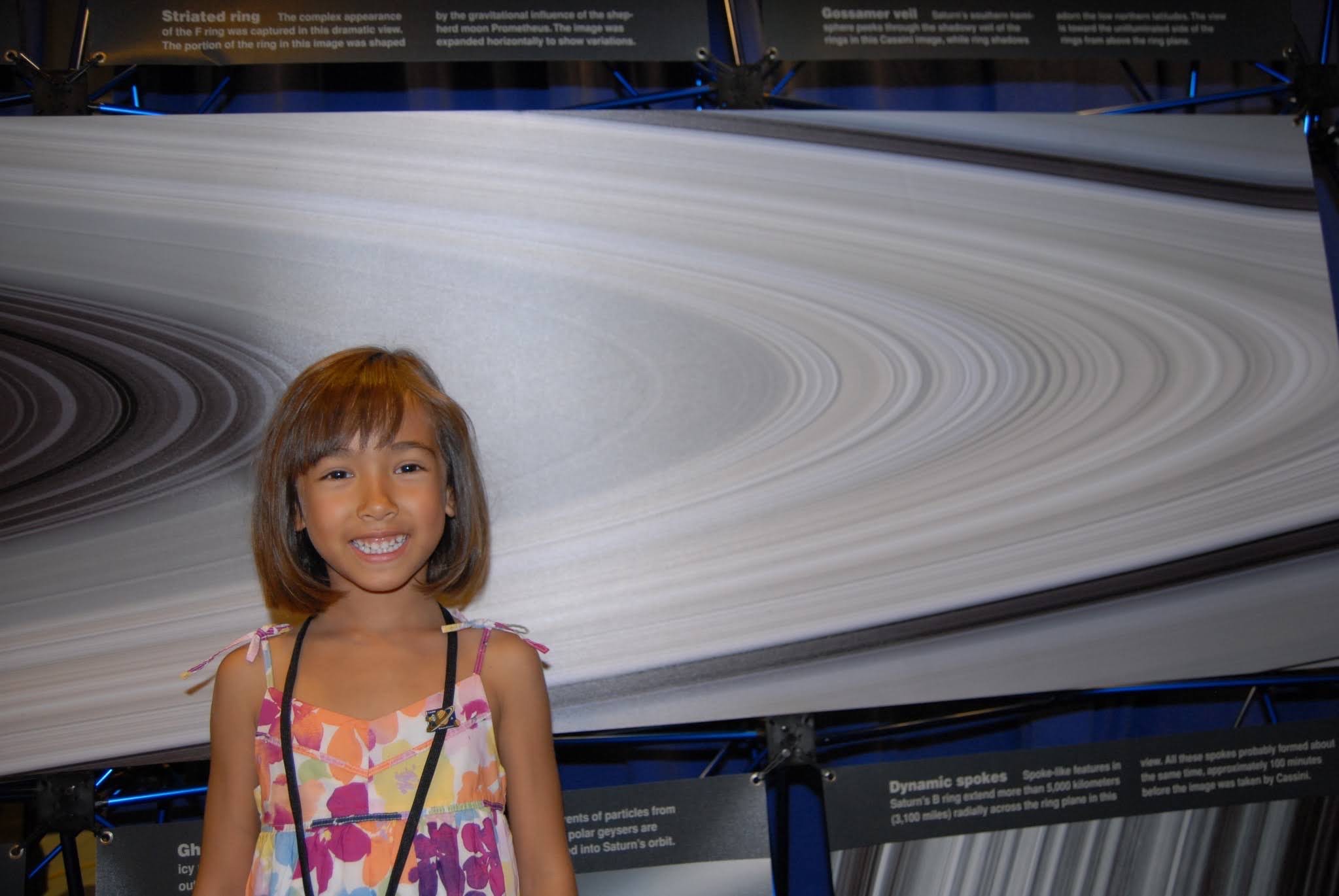A little girl standing in front of a picture of Saturn's rings