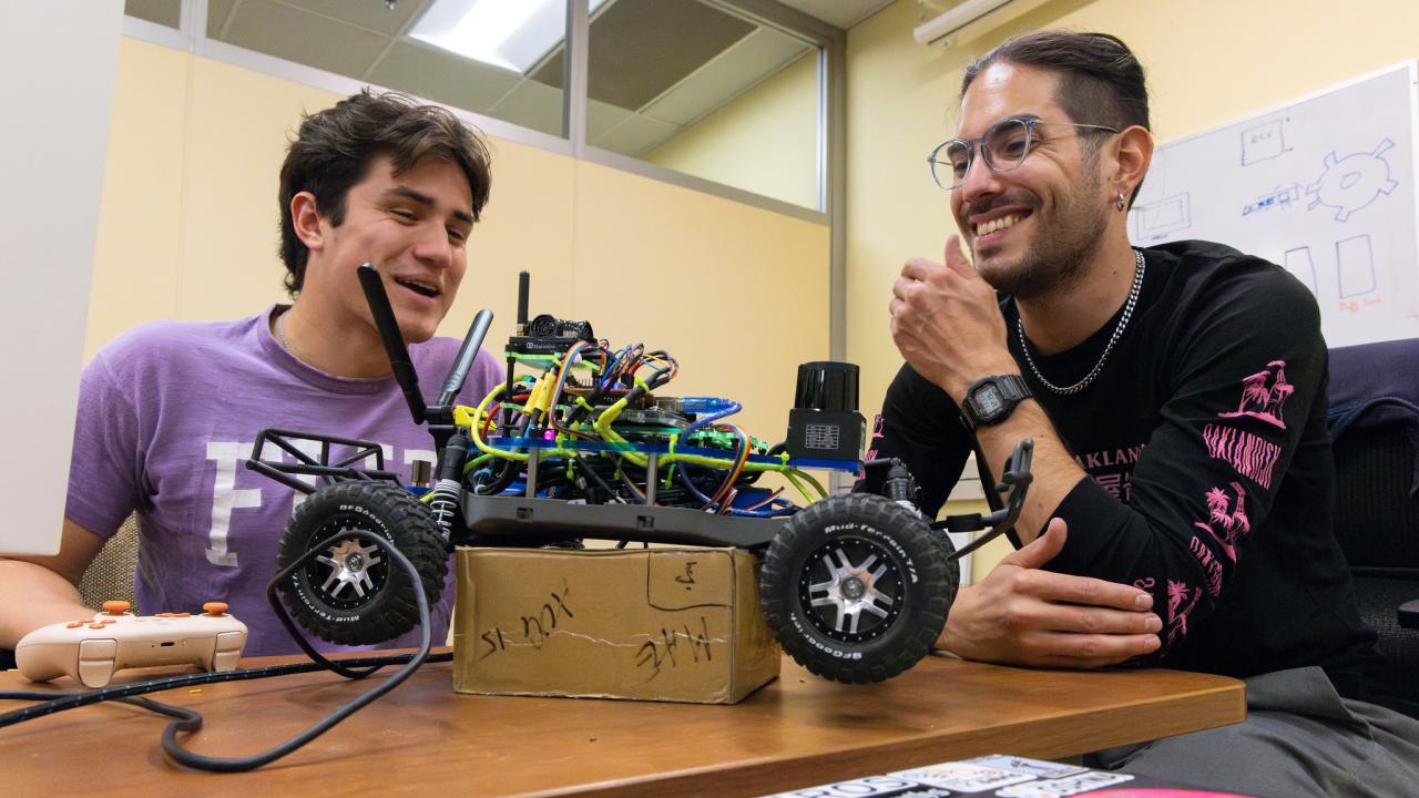 Erik Contreras and other student smile as they look at robotic car on table