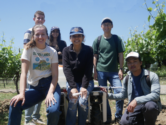 Students stand in field with a robot