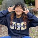 Tichada Tantasirikorn holding up peace signs wearing a UCD sweater