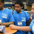 Three students stand together, looking at a laptop